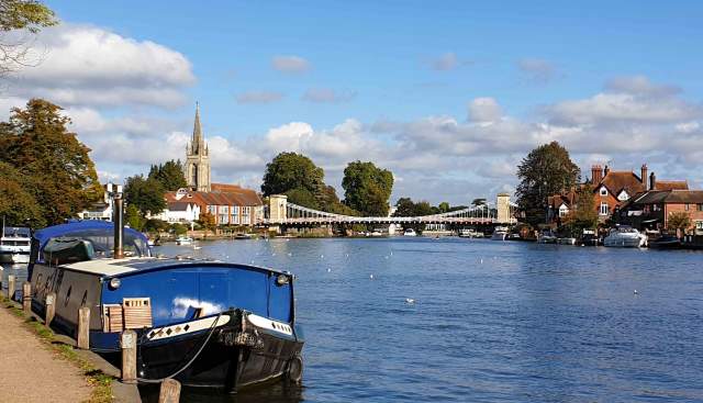 The Thames Path alongside the river Thames with a barge moored and Marlow Bridge and church in the background.