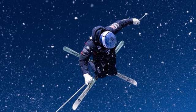 Nick Page in mid-air with skis crossed in an x and snow falling all around
