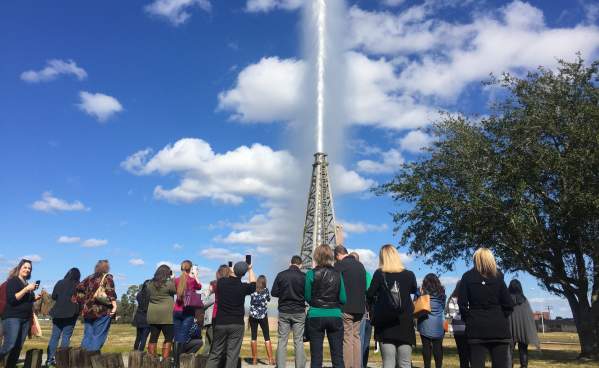 Visitors watch the gusher blow against a blue sky