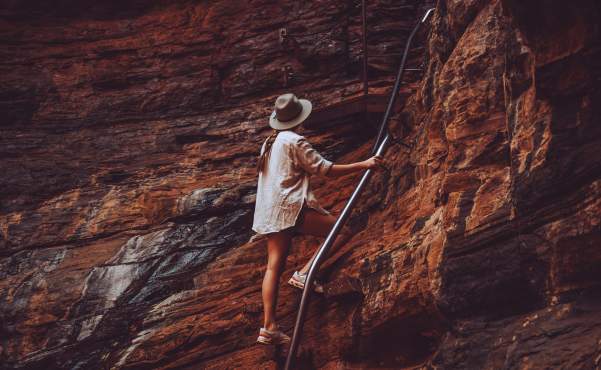 A woman climbs rocks using the handrail at Handrail Pool in Weano Gorge, Karijini National Park