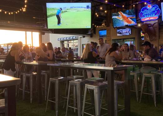 Big screen TV and patrons sitting at high table tops at Little Woodrow's Sports Bar