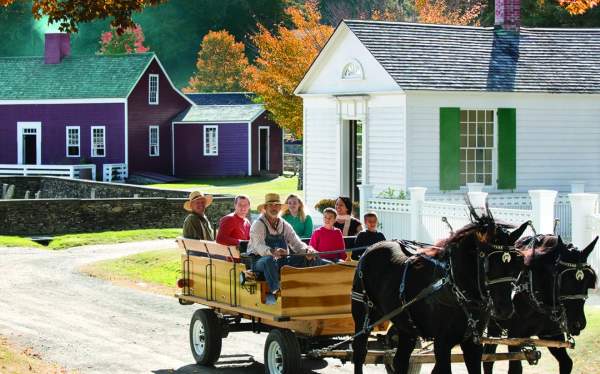 an image of a horse drawn carriage carrying people in front of historic houses with fall leaves behind it