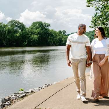 a man and woman walk along a riverside path