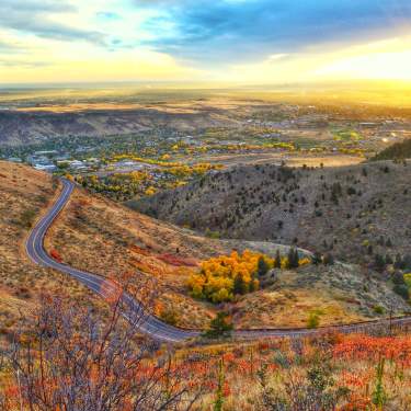 Golden, Colorado, at sunrise, seen from Lookout Mountain Road, with vibrant fall colors of yellow and orange in the foreground.