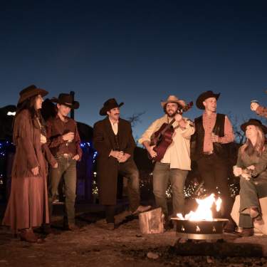 People around a campfire in Golden in western attire, one person is playing a guitar