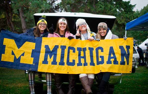 Four women smiling at holding a U-M banner