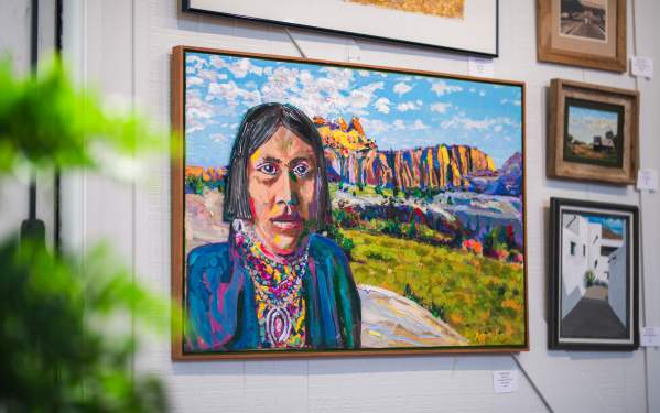 Colorful painting of a native american in the foreground looking at the viewer from a colorful landscape