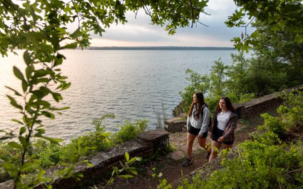 Two women hiking through the Lake Brownwood State park hiking trails with the lake on their right.
