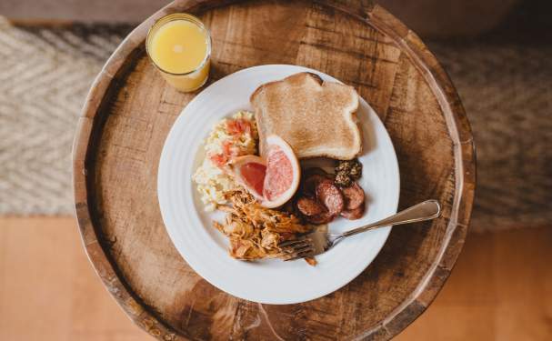 A glass of orange juice sits next to a plate of eggs, toast, grapefruit, and sausage.