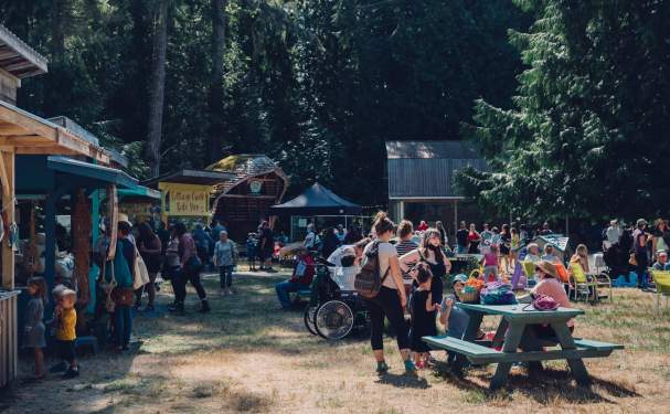 A view of people browsing market stalls and gathering around nearby picnic tables.