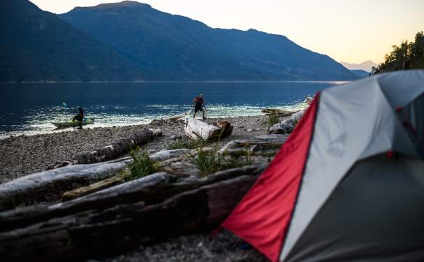 Two people bring their kayaks ashore near their campsite.