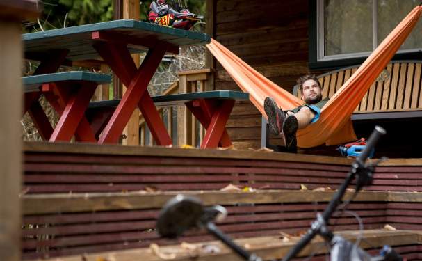 A man relaxes in a hammock with at the lodge with his bike and helmet resting nearby.