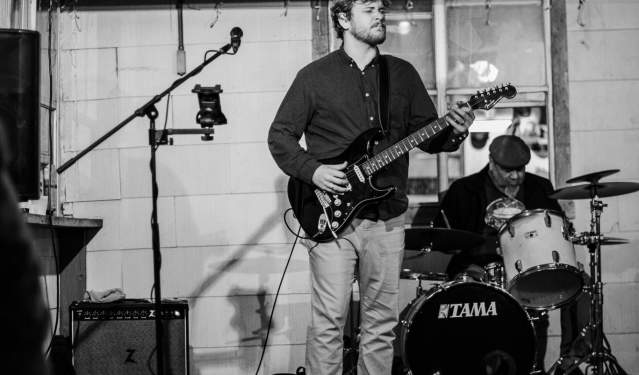 Black and white image of a man singing and strumming a guitar.