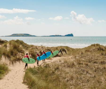 Surfers walking along dunes with their surfboards towards the beach