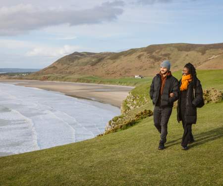 Couple walking along rhossili bay coastline