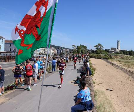 crowd cheering on competitors running along the swansea beach front during the Ironman Swansea event