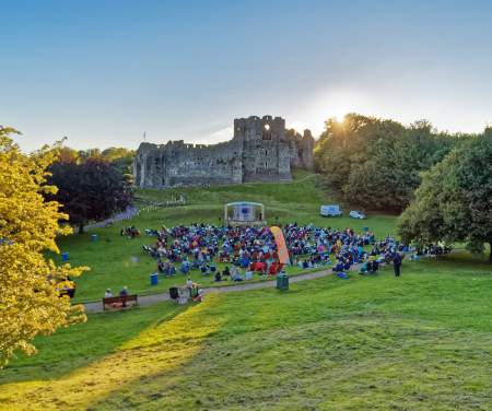 theatre performance with crowd watching on with oystermouth castle in the background at sunset