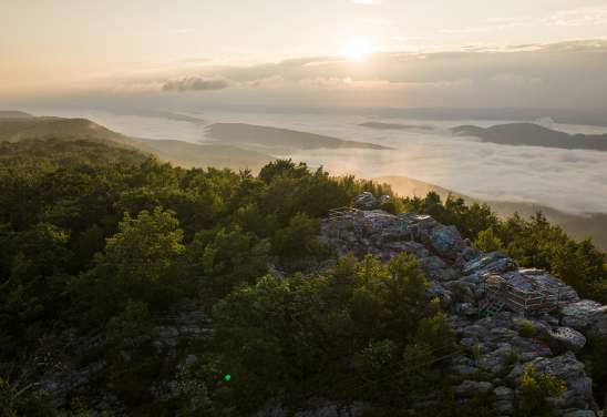 Sunrise over the Appalachian Mountains from Dan’s Rock Scenic Overlook in Dans Mountain State Park, with a rocky viewing platform surrounded by forest and a valley filled with morning fog.