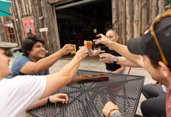 A group of adults sit around a table, holding up glasses of beer to cheers eachother.