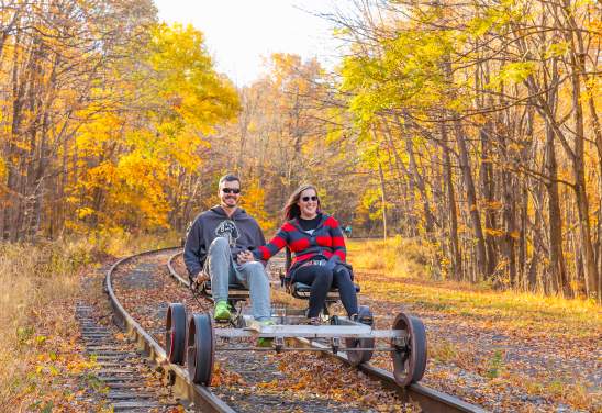 A couple peddles on a rail bike riding along the rail line in the fall.