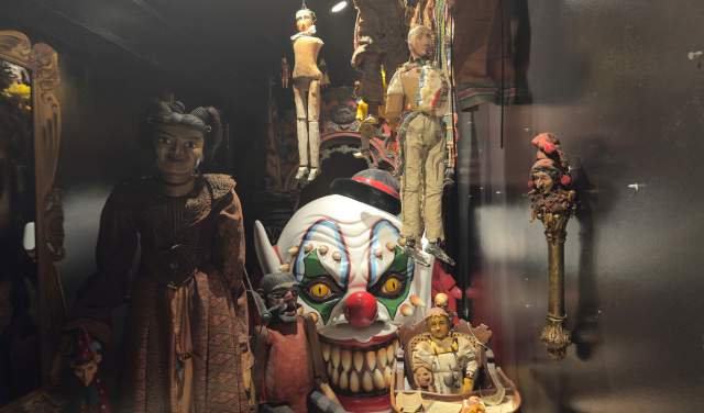 Creepy dolls and a clown head in a display case in a museum