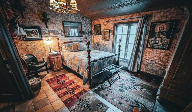 A creepy room inside Farnsworth House in Gettysburg with a full bed with plaid bedding, vintage photographs, and a chandelier light made out of antlers