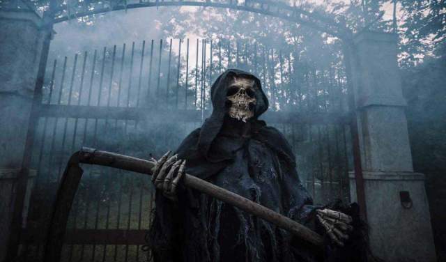 A reaper standing in front a a large gate with fog