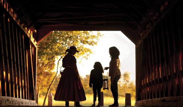 Silhouettes of two adults and a child standing on an old bridge with the sun shining through