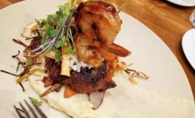 A fancy meal in layers: mashed potatoes on the bottom, a meant on top, and some shrimp on the top of that, garnished with some greens
