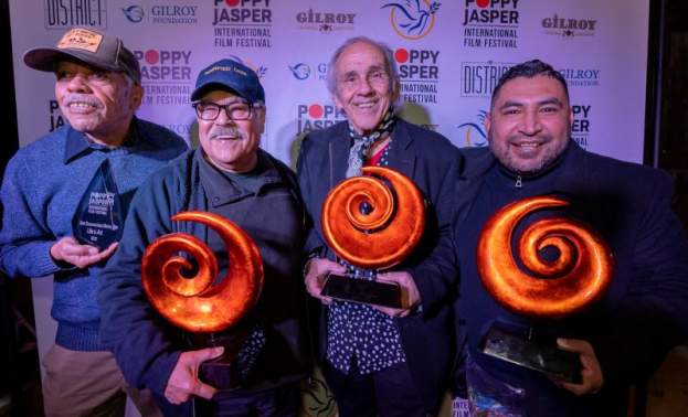 Four men holding orange swirl-shaped awards in front of a Poppy Jasper Film Festival labeled backdrop