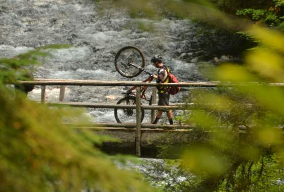 Mountain biker walking bike across bridge.