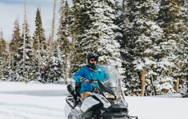 People riding snowmobiles through snowy forest landscape near Brian Head and Cedar City