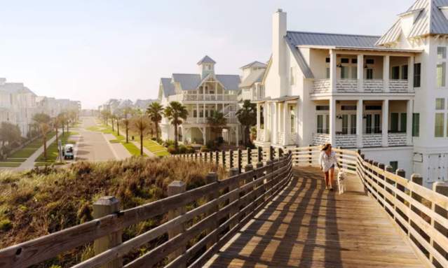 Women walking down a board walk with a white house in the back