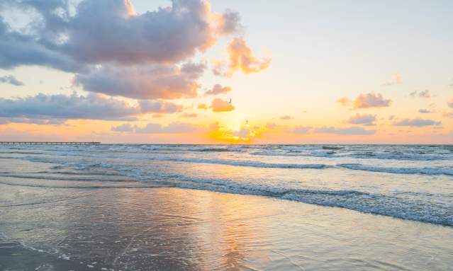 A bright, golden sunrise over the ocean waves on a beach in Port Aransas.