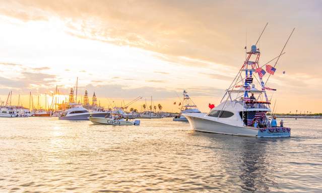 Several boats, decorated in various theme, head away from the camera