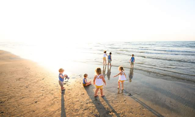 A group of seven kids of various ages play on the beach in coordinating yellow and blue outfits