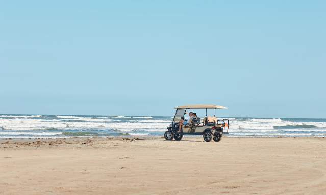 A golf cart sits on the beach in the distance with waves crashing behind.