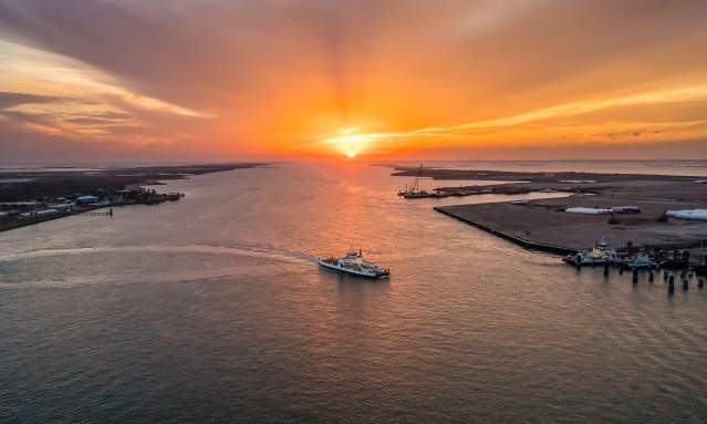 Ferry boat crossing over from one side to the other. Sun setting with orange and yellow colors spreading through the sky.