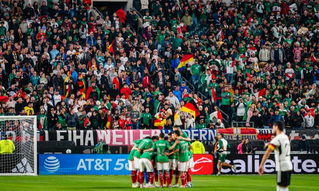 A huddle of soccer players in front of a goal in a crowd-filled stadium