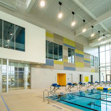 Interior view of the James A. Leach Aquatics and Recreation Center competition pool, featuring lane dividers, starting blocks, tall windows, and colorful acoustic panels along the upper wall.