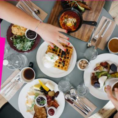 Overhead view of a shared brunch table with waffles, eggs, coffee, and breakfast dishes being served