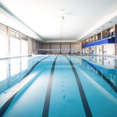 Indoor competition pool at Methodist University with clear blue water, lane markings, lifeguard chairs, and large windows and balcony seating along the upper level.