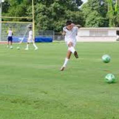 Children practice soccer on a grassy field, with one player kicking a ball while others watch and participate in drills.
