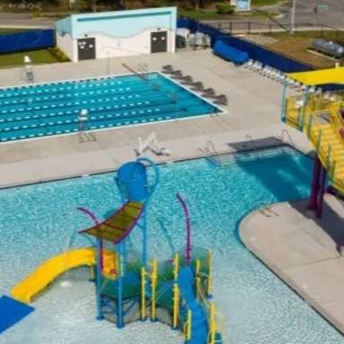 Aerial view of the Lake Rim Aquatic Center showing a lap pool with swim lanes, adjacent shallow play pool, colorful water slides, and splash features on a sunny day.