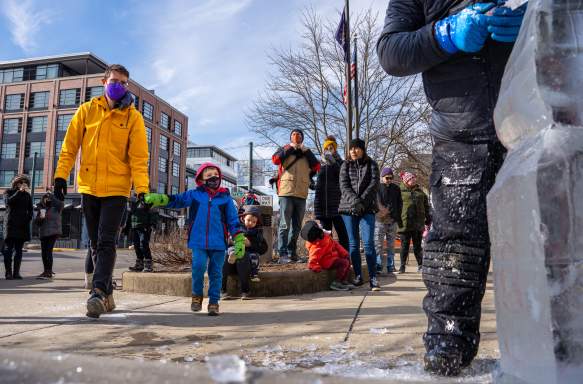 A dad holding his small son's hand as they approach a live carving demonstration during Freezefest