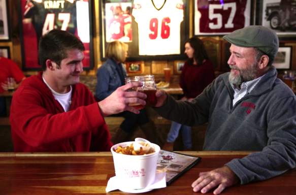 Two men cheers-ing beers with a bowl fries at Nick's English Hut