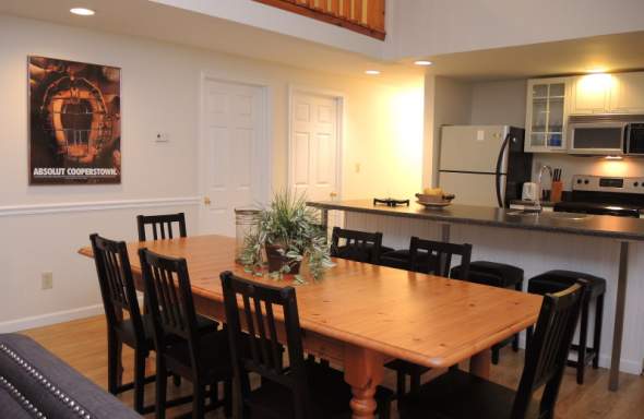 An empty dining room with a wooden table, black chairs and a kitchen in the background..