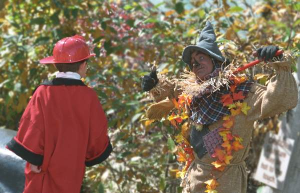 Scarecrow hanging in a field with child dressed as fire fighter looking over at him at the Columbus Zoo