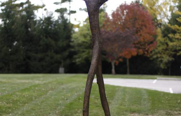 Bronze stick figure sculpture with branches coming out of the head.