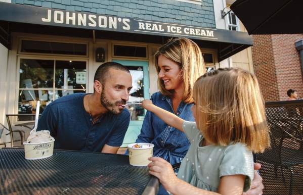 A young daughter feeding ice cream to her dad while her mom watches on the front patio of  Johnson's Ice Cream